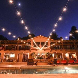 Elegant evening scene with string lights over a pool and a warm-lit building.
