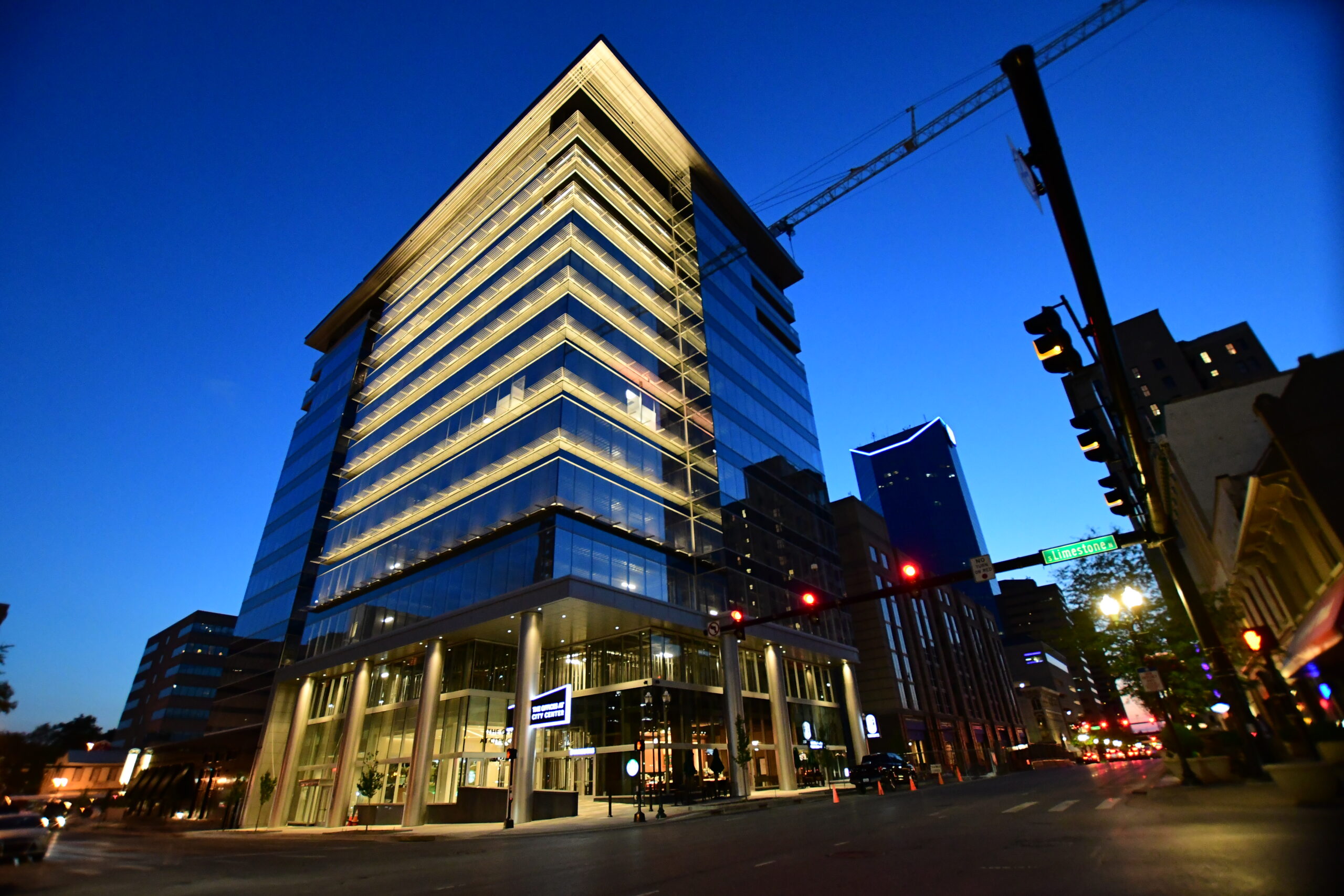 Modern glass office building illuminated at night with a city skyline backdrop.