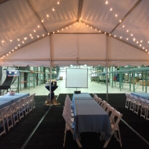 A large event tent with string lights and tables set for a gathering.
