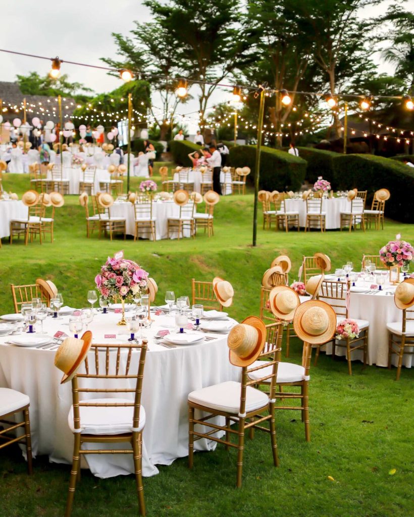 Elegant outdoor wedding reception with beautifully decorated round tables and string lights.